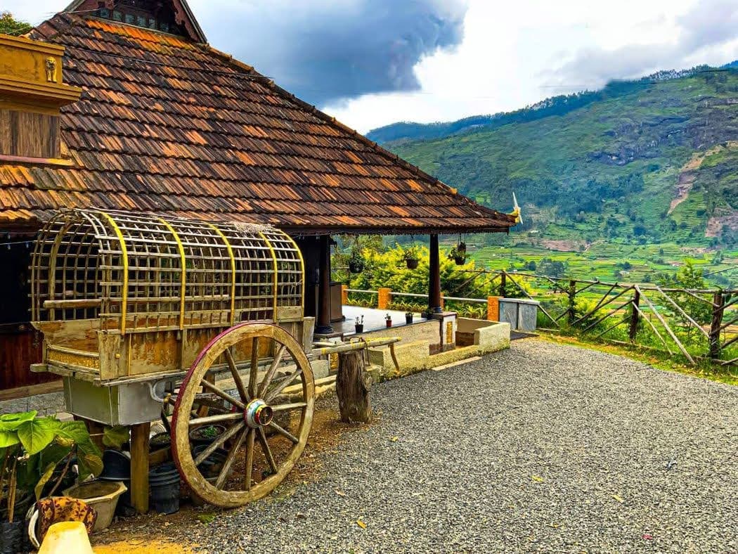 Traditional wooden cart parked beside a tiled house overlooking lush green terraced mountain slopes.
